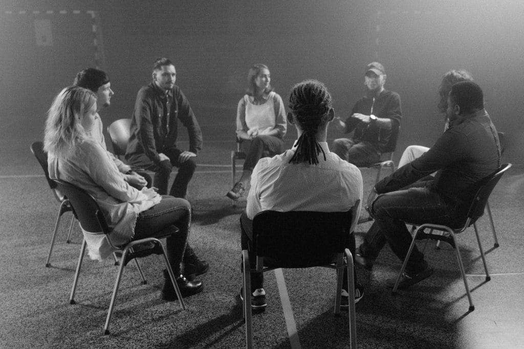 A diverse group of people in a circle discussing and supporting each other in a therapy session.